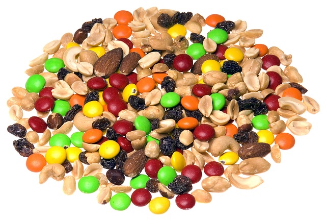 Colorful trail mix with peanuts, almonds, raisins, and candy-coated chocolate pieces on a white background.